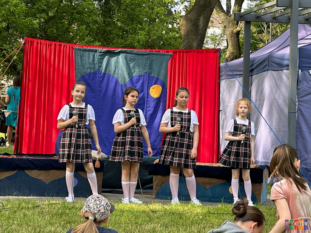 Zdjęcie przedstawiające cztery dziewczyny trzymające mikrofony. Za nimi tak jak by jakaś dekracja - zasłonka czerwono niebieska