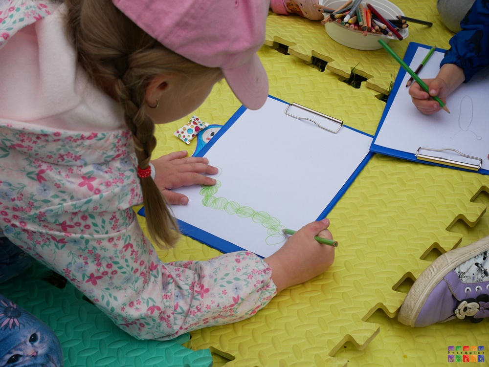 Zdjęcie przedstawiające rysującą dziewczynkę obrazek na kartce papieru.
