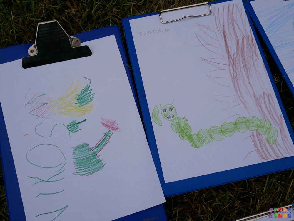 Zdjęcie przedstawiające 3 obrazki narysowane na kartkach papieru i leżące na trawniku