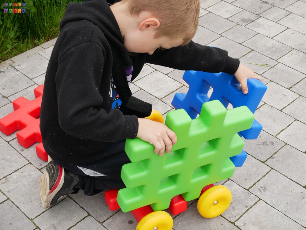 Zdjęcie przedstawiające dziecko układające coś z klocków. W tle kawałek trawnika oraz kostka brukowa