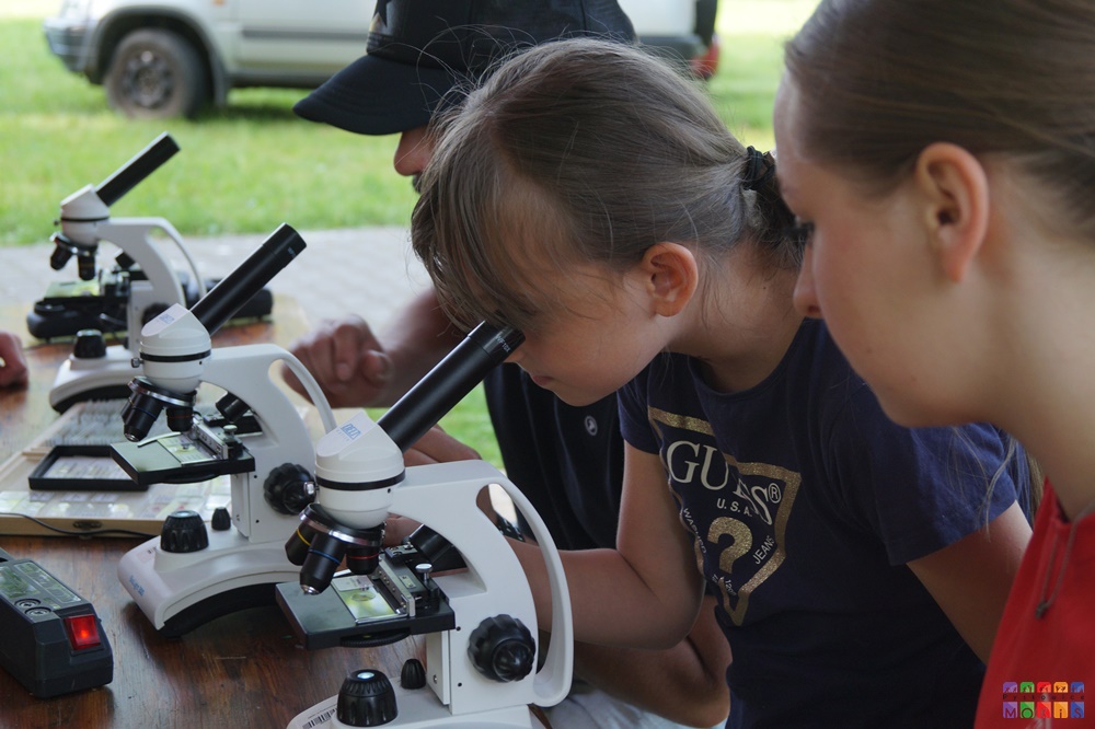 Zdjęcie przedstawiające dwoje dzieci patrzących przez mikroskop stojący na stoliku.