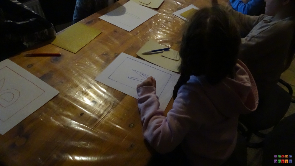 Zdjęcie przedstawiające dziecko siedzące przy blacie stołu na którym znajdują się kartki papieru
