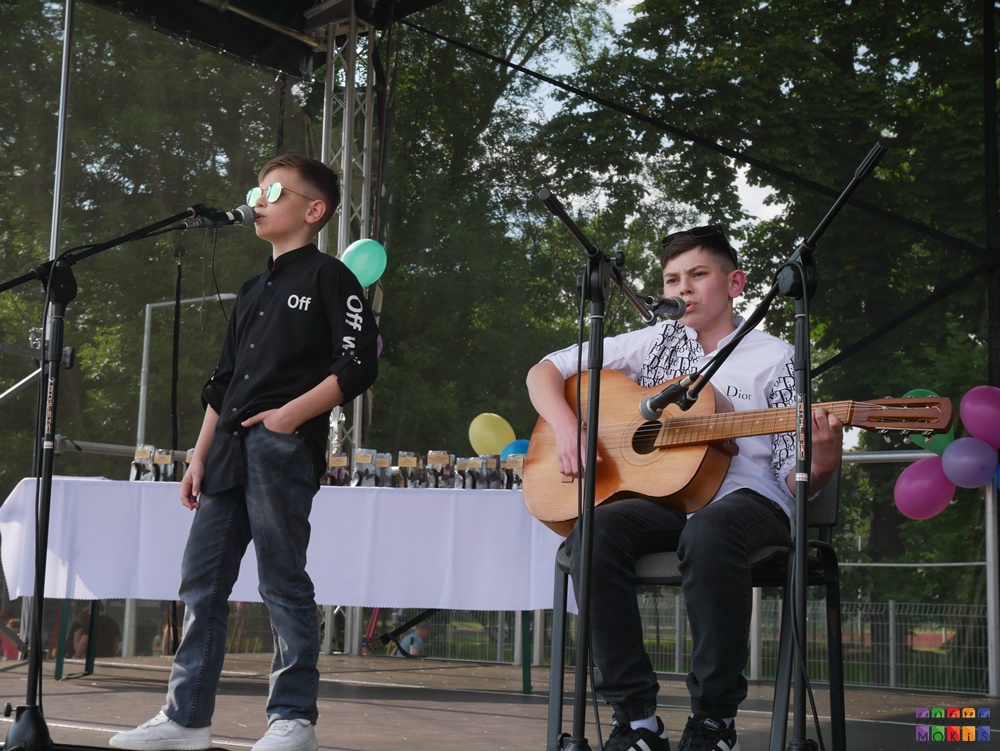 Zdjęcie przedstawiające śpiewające dzieci do mikrofonów. Jedno z nich gra na gitarze