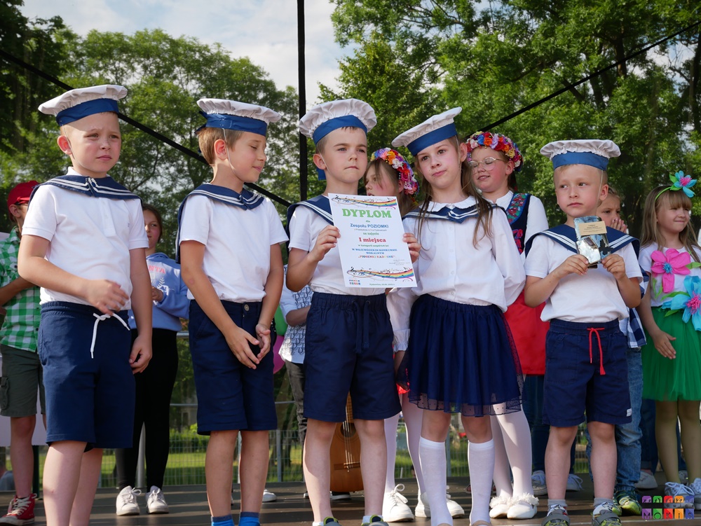 Zdjęcie przedstawiające stojące dzieci z dyplomem i statuetką w ręku. Za nimi stoją inne dzieci.