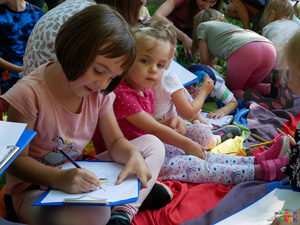 Zdjęcie przedstawiające siedzące dzieci i rysujące na kartkach papieru.