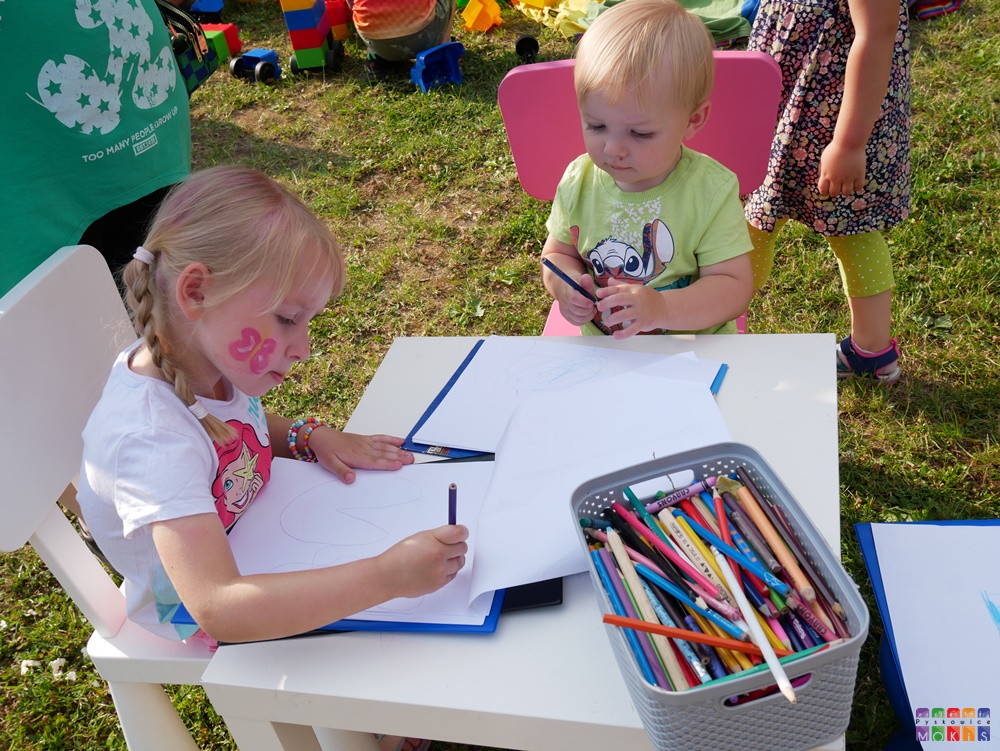 Zdjęcie przedstawiające siedzące dziecko przy stoliku na którym coś rysuje