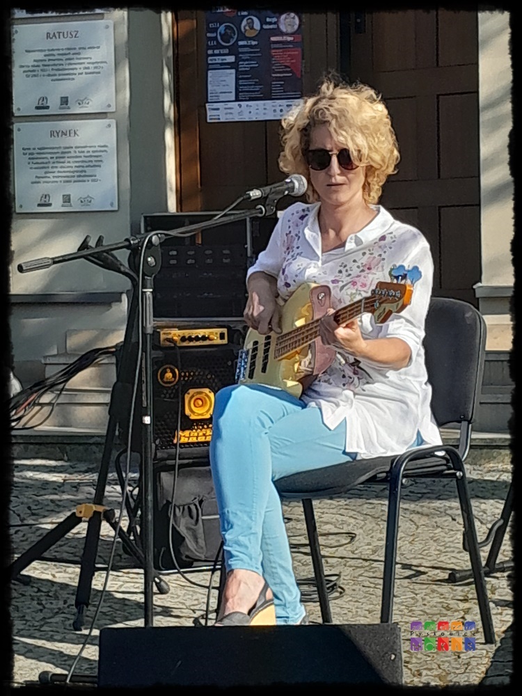 Zdjęcie przedstawia siedzącą na krześle kobietę grającą na gitarze.