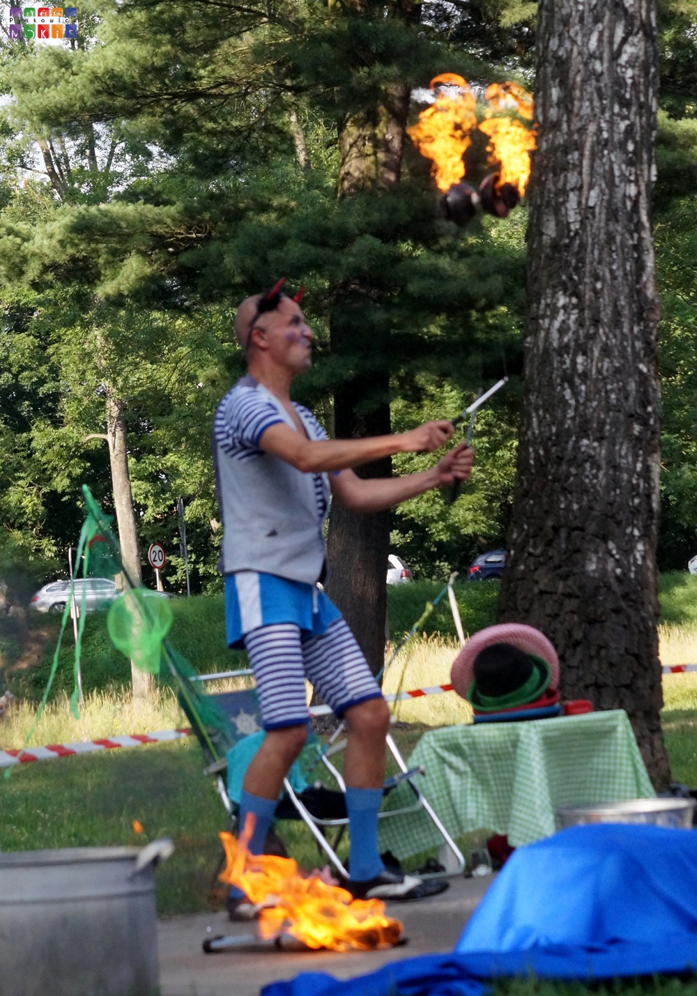 Zdjęcie przedstawia żaglującego mężczyznę płonącym przedmiotem. W tle widać drzewa parkowe.