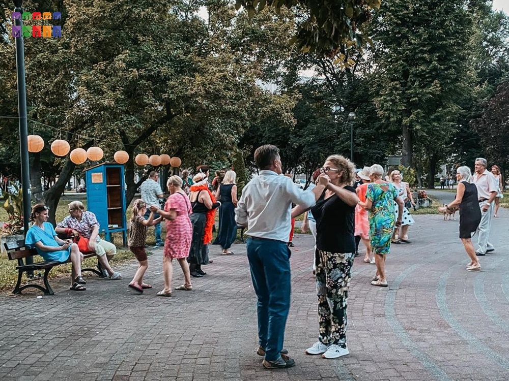 Zdjęcie przedstawiające tańczących ludzi w parku. W tle widać drzewa parkowe.