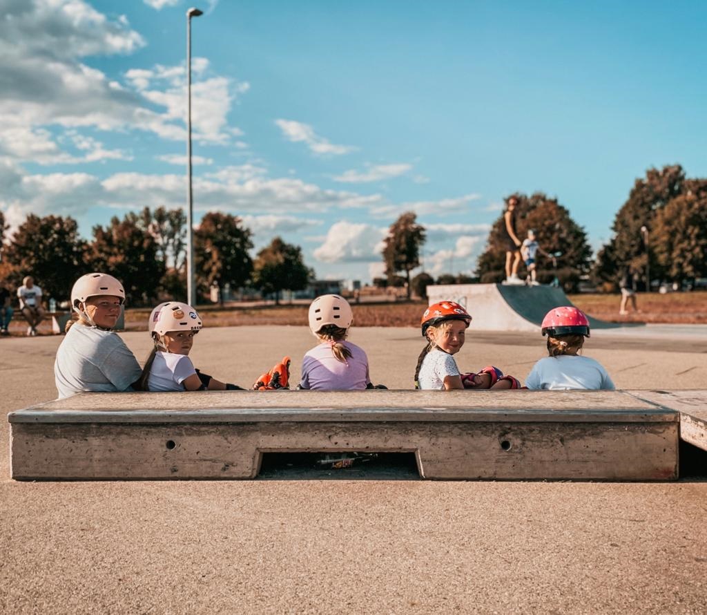 Zdjęcie przedstawia siedzących dzieci za podestem z głowami obróconymi w kierunku fotografa. Na głowach mają założone kaski