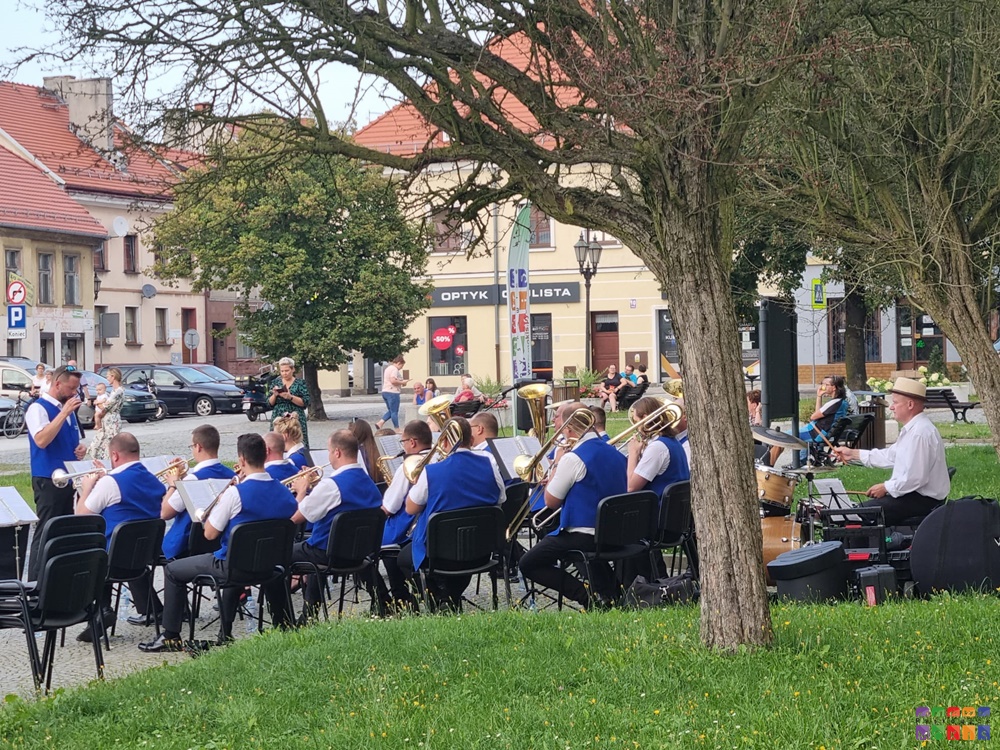 Zdjęcie przedstawia grającą orkiestrę dentą na rynku w Pyskowicach. W tle widać kamienice