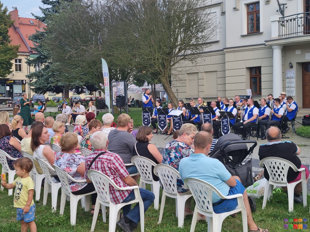 Zdjęcie przedstawia grającą orkiestrę dentą przed Ratuszem w Pyskowicach. Po lewej stronie widać siedzących ludzu.