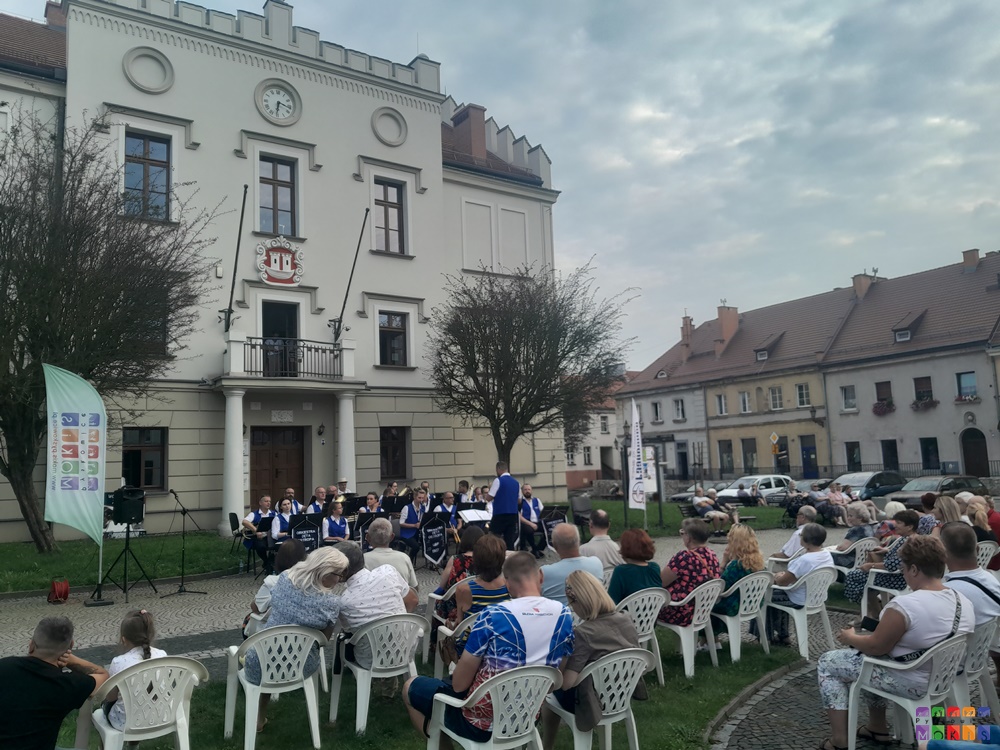 Zdjęcie przedstawia grającą orkiestrę dentą przed Ratuszem w Pyskowicach oraz siedzących na krzesłach ludzi