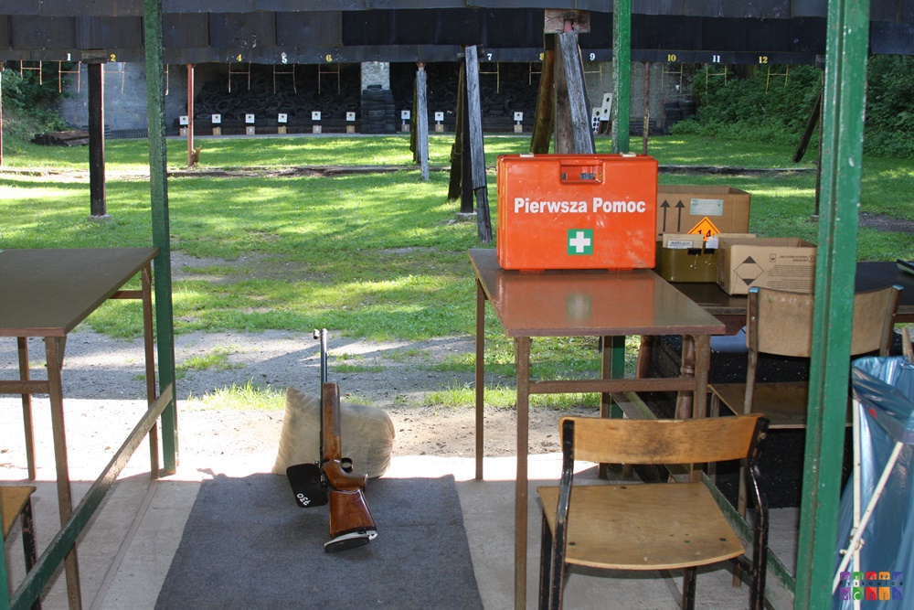 Zdjęcie przedstawiające strzelnicę sportową. na pierwszym planie broń długa po prawej stronie widoczna apteczka
