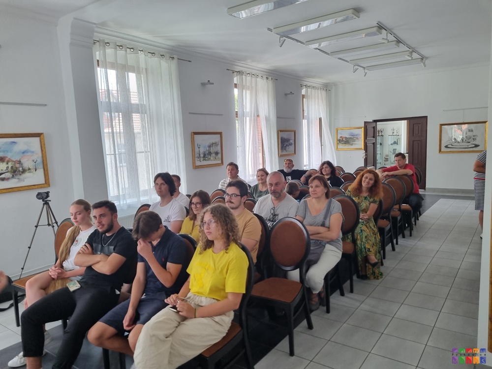 Zdjęcie przedstawia grupę ludzi siedzących na krzesłach w pomieszczeniu sala ślubów w Ratuszu w Pyskowicach