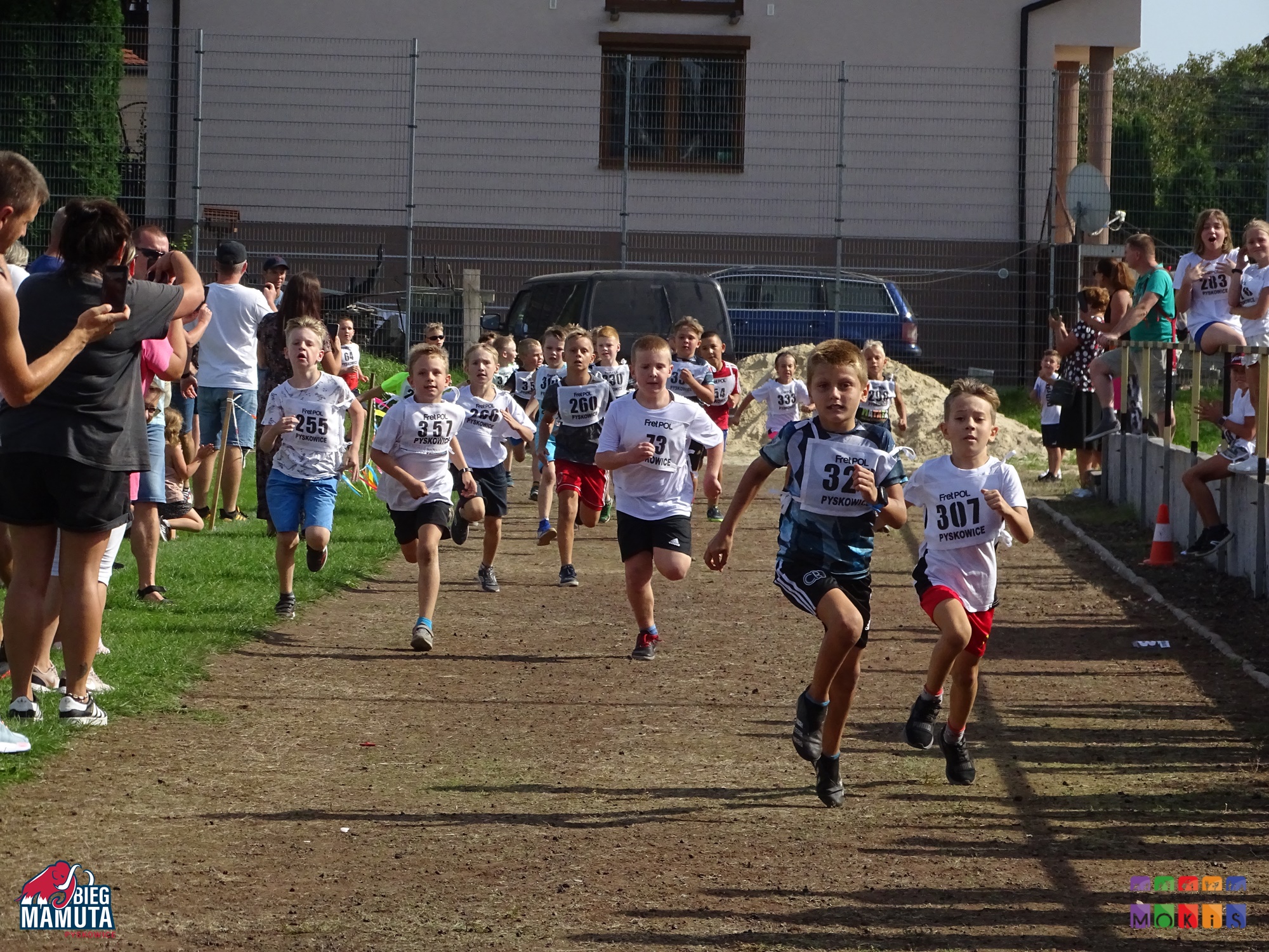 Zdjęcie przedstawia biegnące dzieci na bieżni boiska