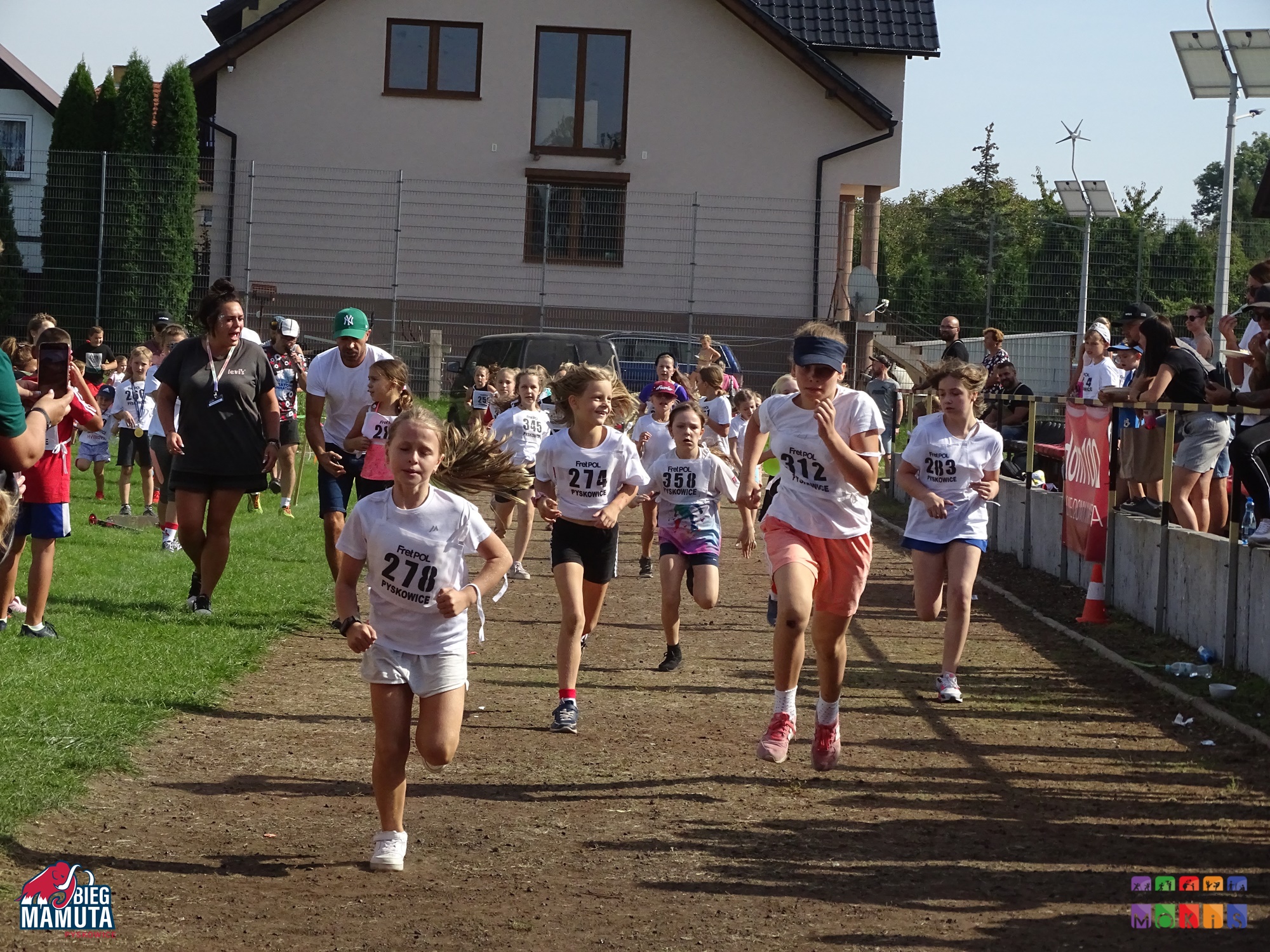 Zdjęcie przedstawia biegnące dzieci na bieżni boiska