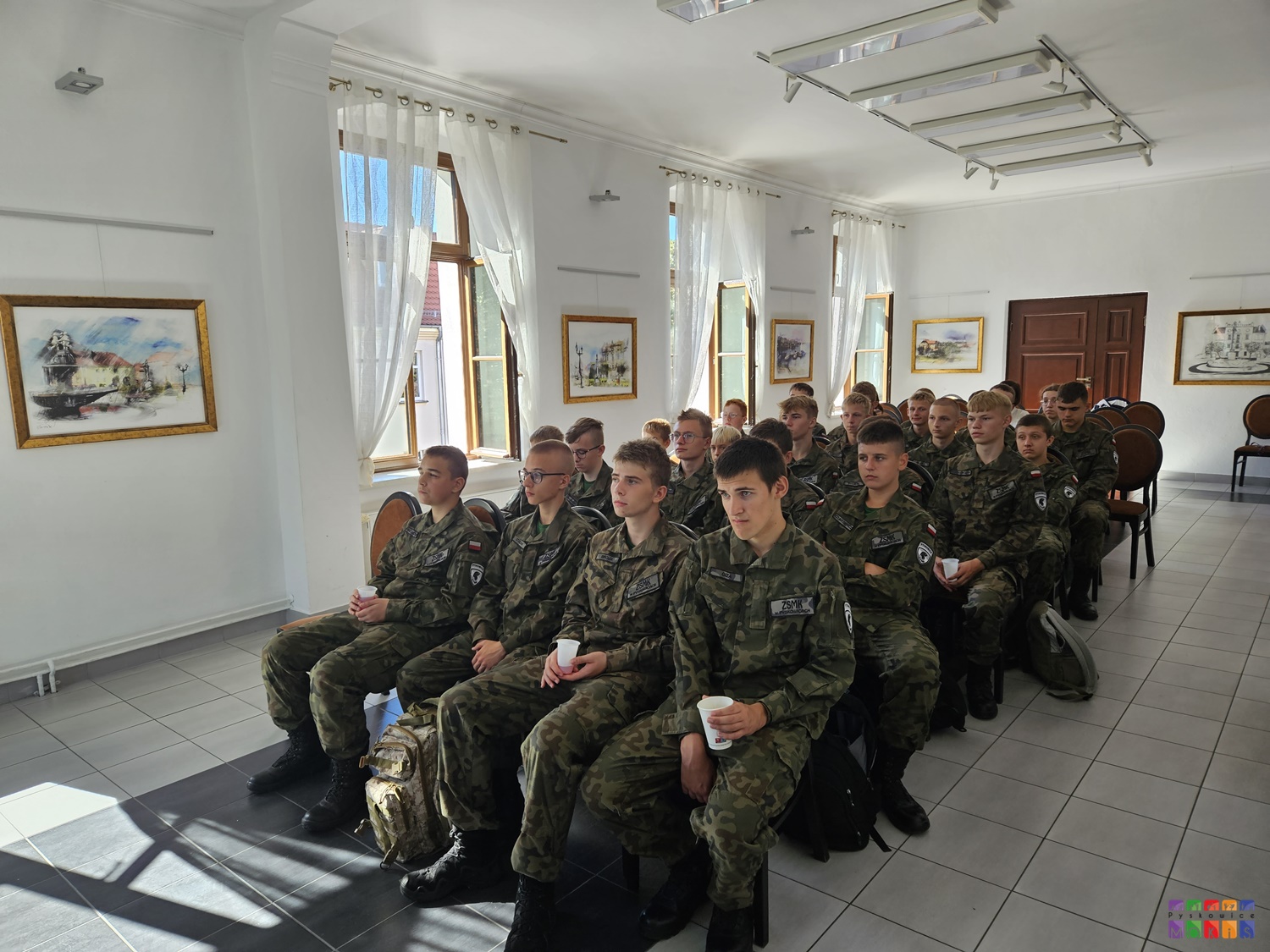 Zdjęcie przedstawia siedzących ludzi w mundurach na krzesłach w sali Centrum Wystawienniczego w Pyskowicach