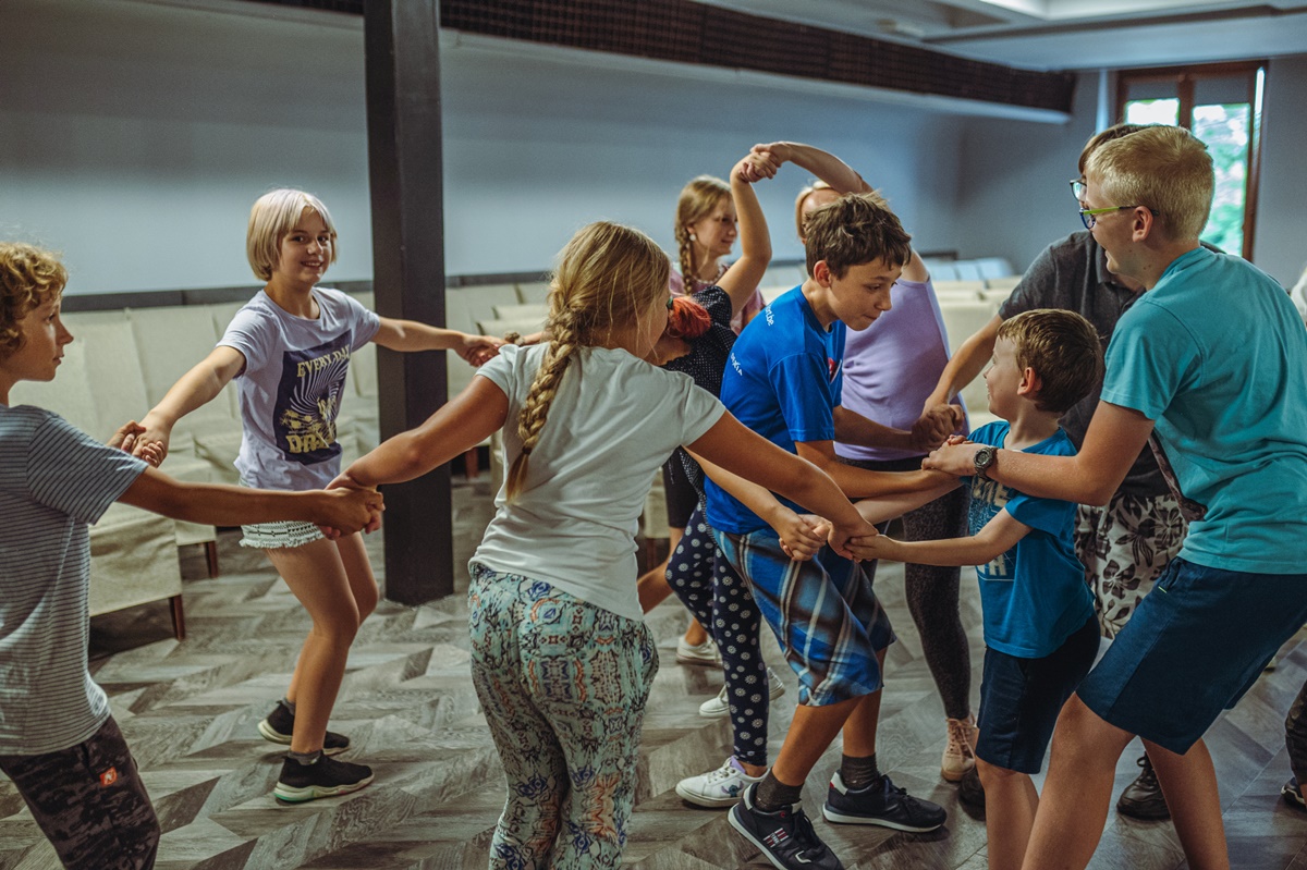Zdjęcie przedstawiające tańczące dzieci w sali widowiskowej MOKiS Pyskowice. Wszyscy trzymają się za ręce.