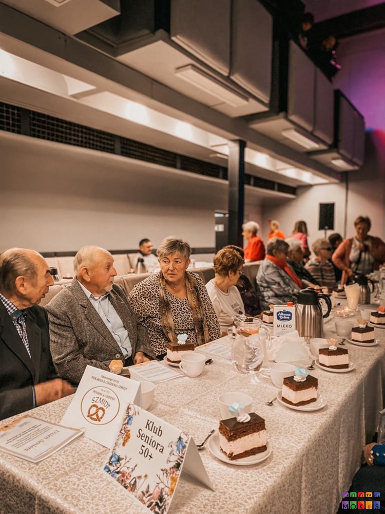 Zdjęcie przedstawiające siedzących seniorów przy stolikach w sali widowiskowej MOKiS