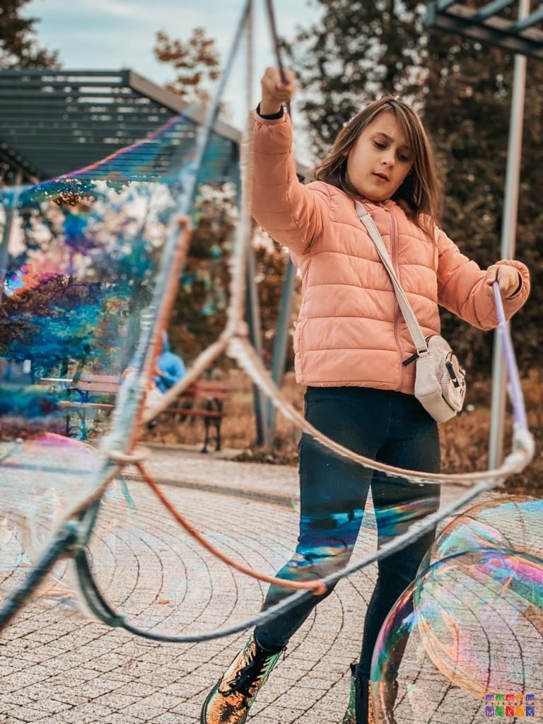 Zdjęcie przedstawiające dziewczynkę robiącą bańki mydlane sznurkami.