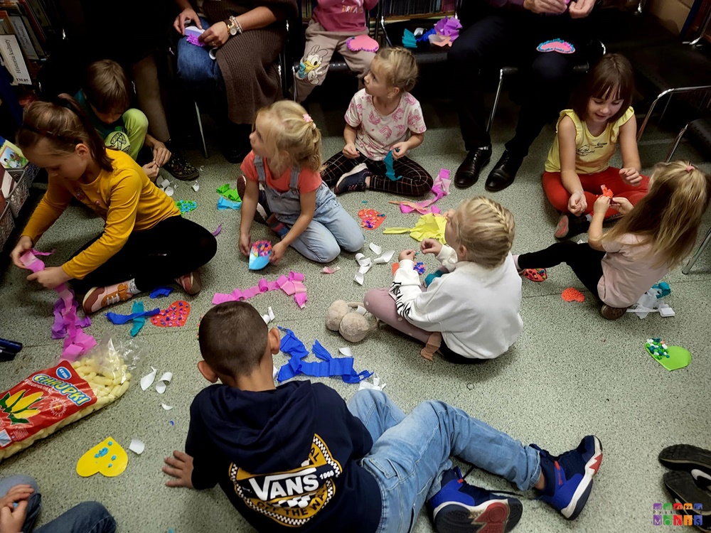 Zdjęcie przedstawiające siedzące dzieci na podłodze wśród rozrzuconej bibuły.