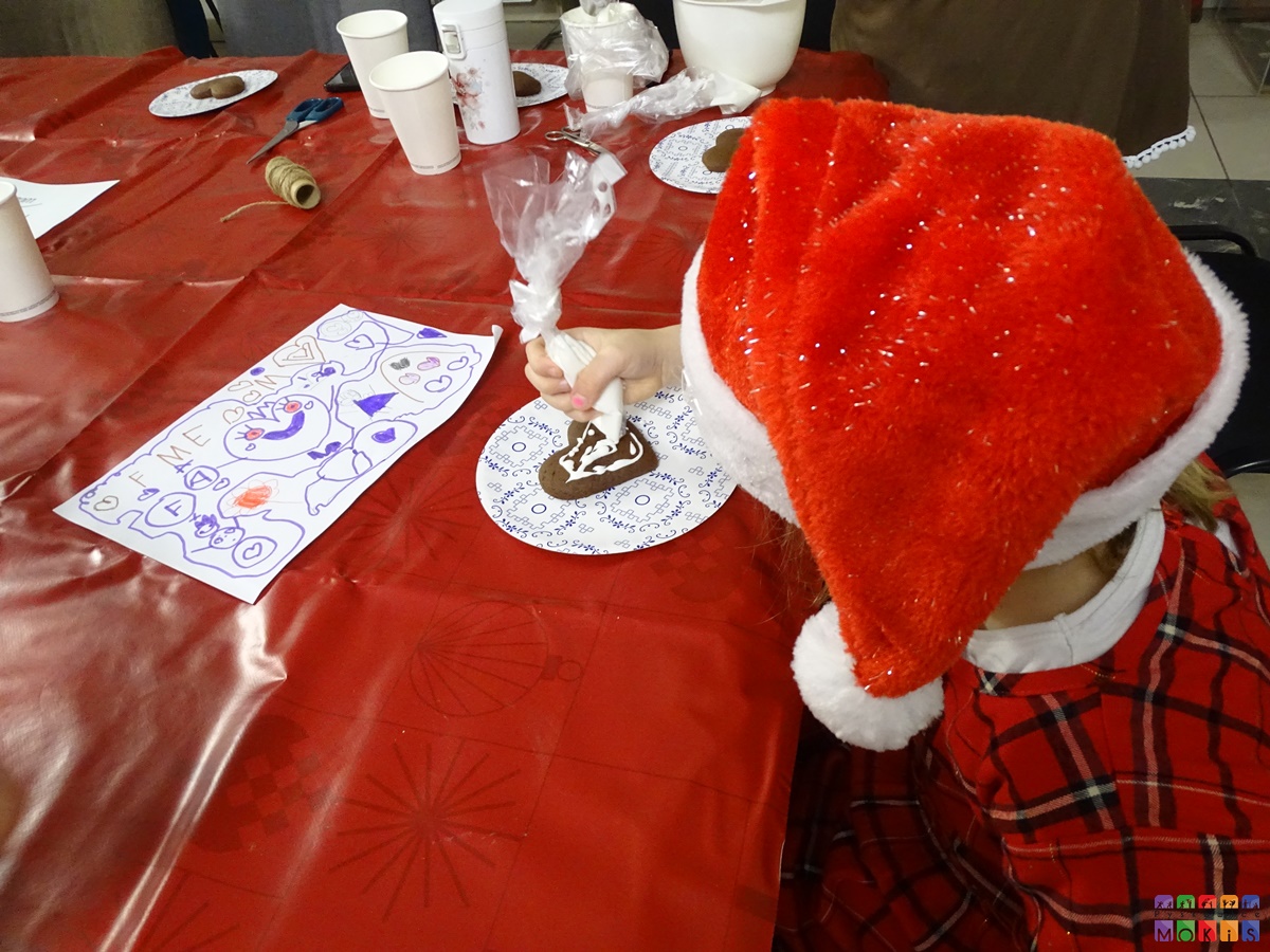 Zdjęcie przedstawia dziecko lukrujące piernika przy stole. Ma ono ubraną czapkę Mikołaja