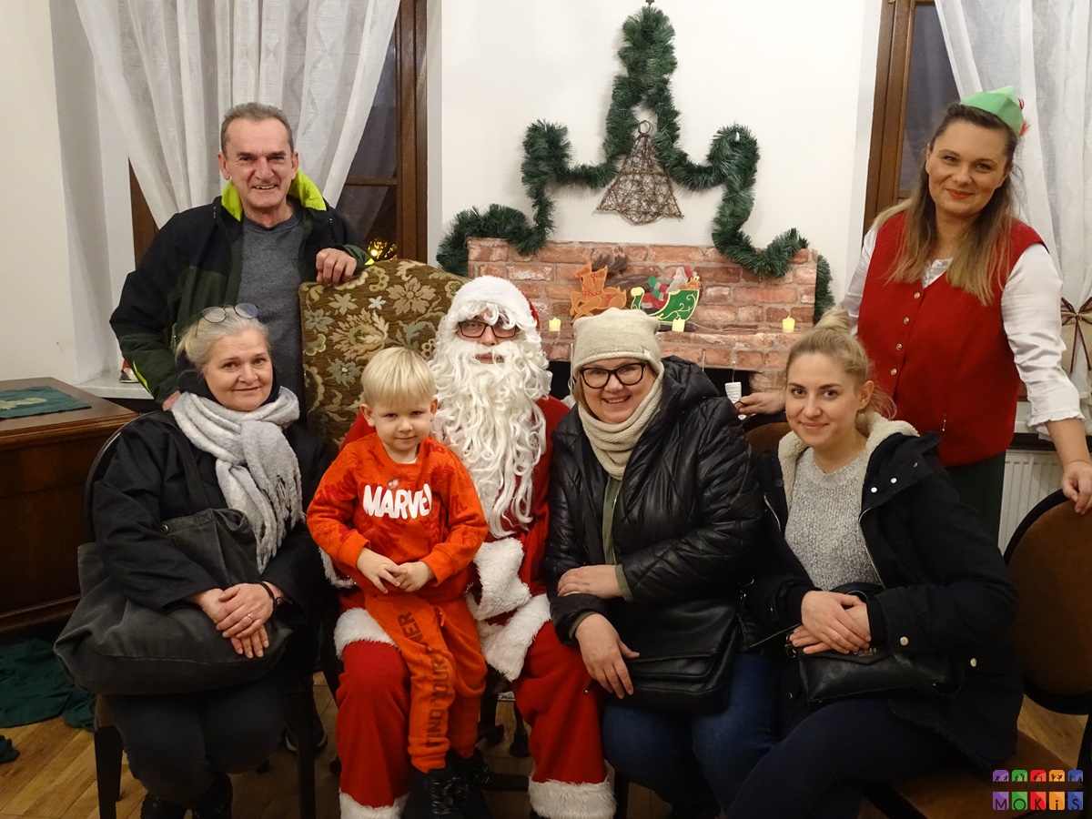 Zdjęcie grupowe z Mikołajem na tle kominka i ozdób świątecznych