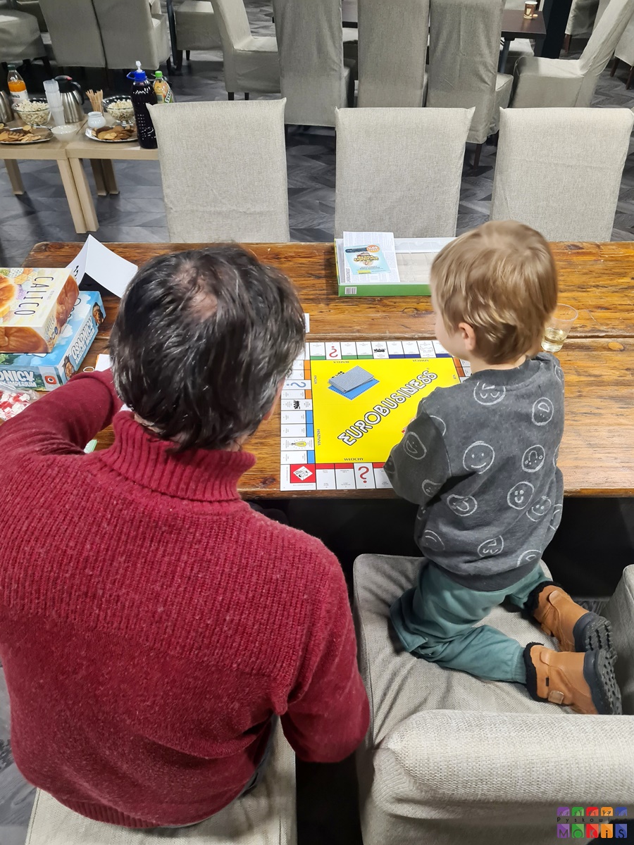Zdjęcie przedstawia siedzącego mężczyznę z dzieckiem przy stole na którym rozłożona jest gra Eurobusiness