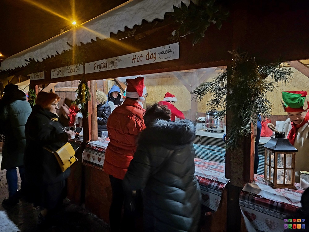 Zdjęcie przedstawiające stragan z ozdobami świątecznymi a przed nim stojących ludzi i oglądających.