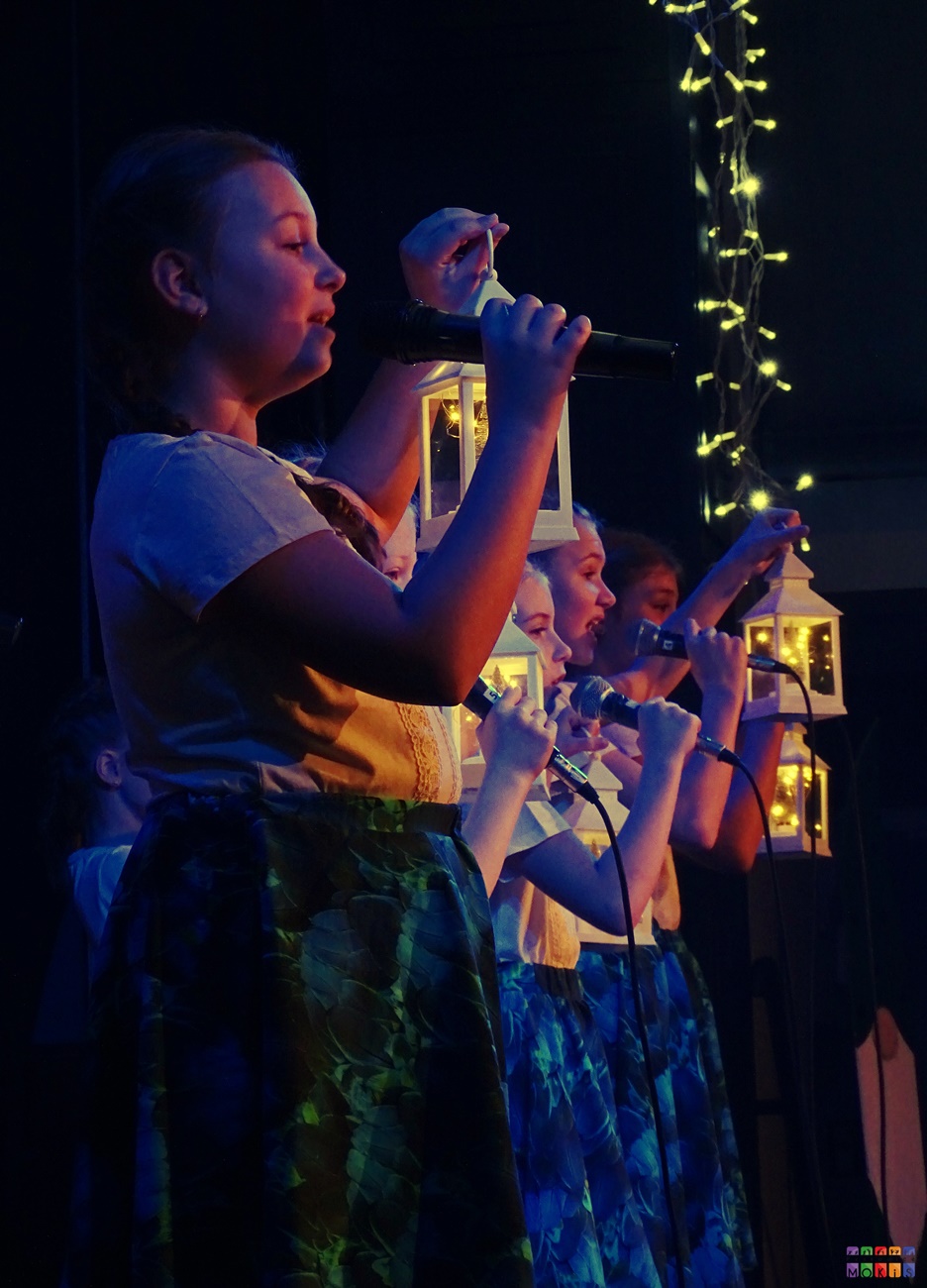 Zdjęcie przedstawia śpiewające do mikrofonów dziewczyny. W rękach trzymają lampiony.
