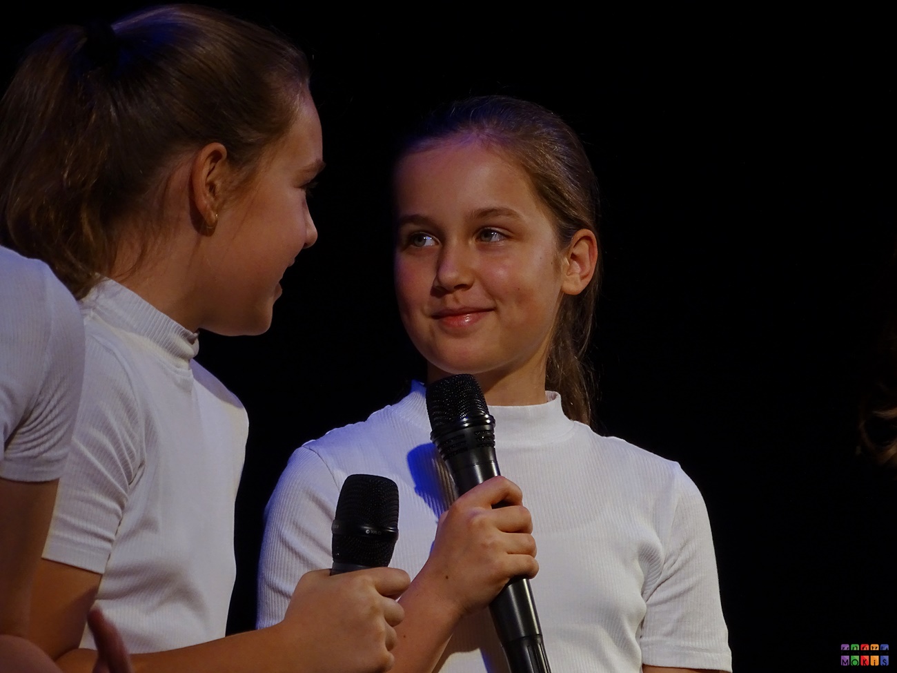 Zdjęcie przedstawia dwie dziewczyny z mikrofonem w ręku patrzące na siebie.