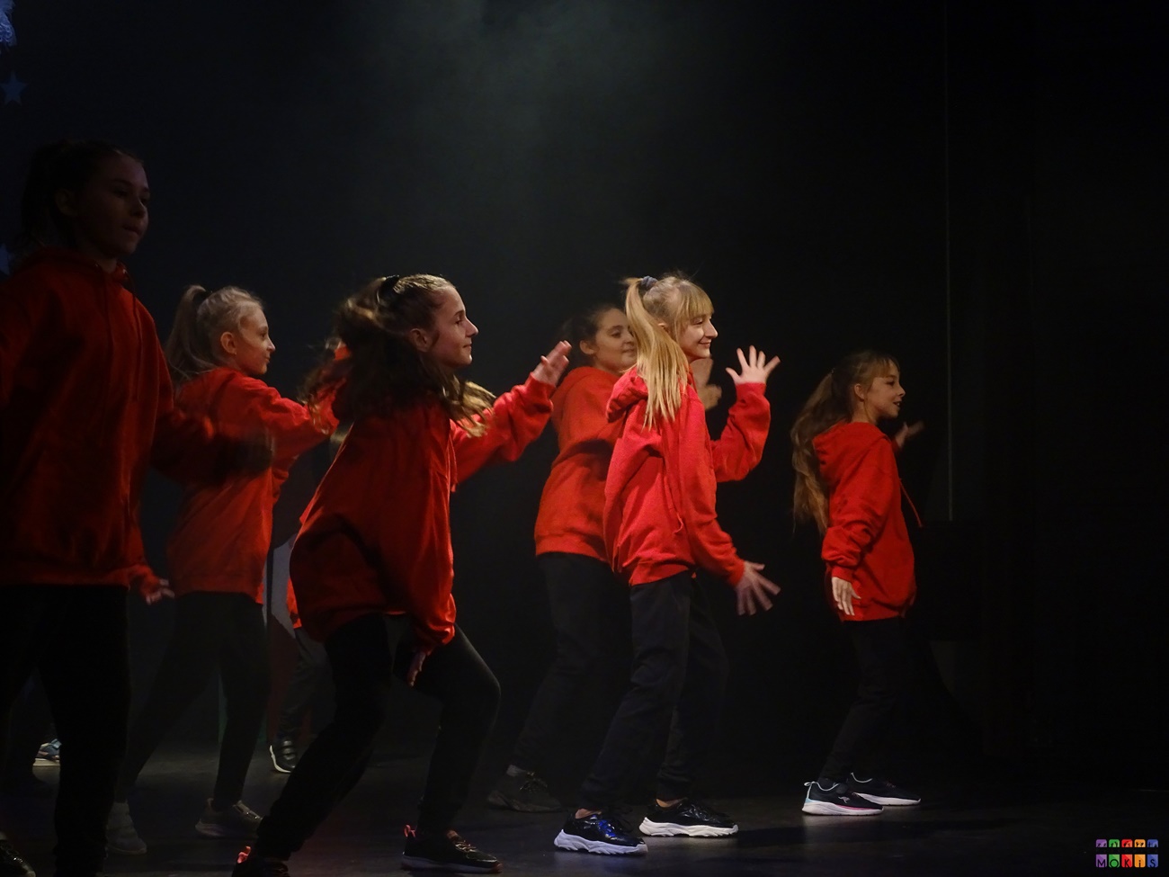 Zdjęcie przedstawia tańczące w czerwonych bluzach dziewczyny na scenie.