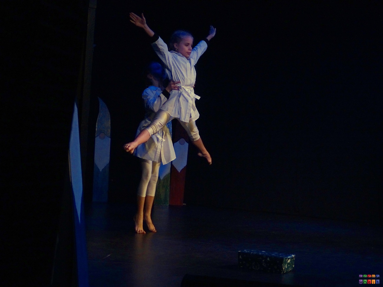 Zdjęcie przedstawia tańczące dziewczyny na scenie. jedna z nich jest uniesiona w górze z rękami wystawionymi do góry