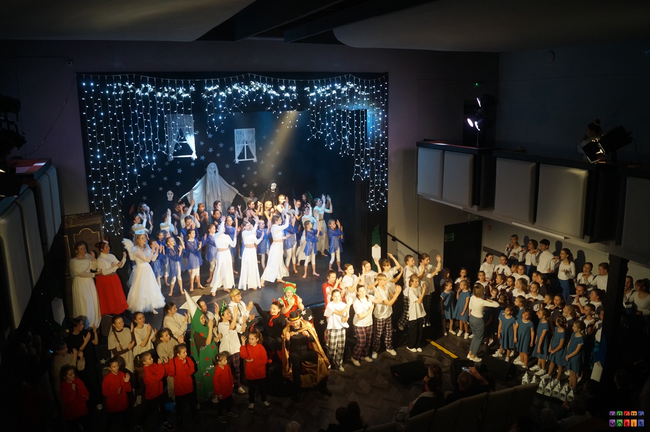 Zdjęcie przedstawia ogólny widok na scenę z wszystkimi tancerzami i wokalistami oraz instruktorami biorącymi udział w koncercie świątecznym. Są oni oświetleni.