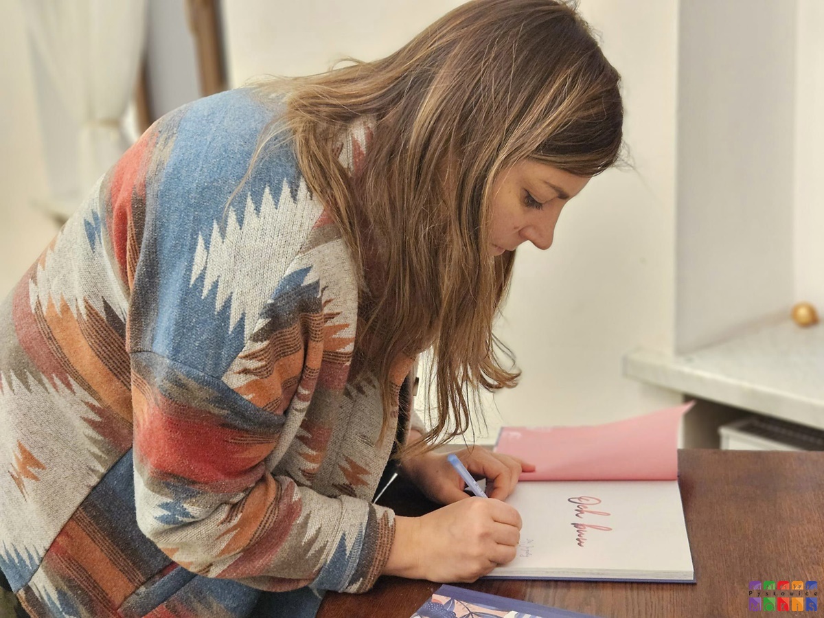 Zdjęcie przedstawiające podpisującą książkę przez kobietę.