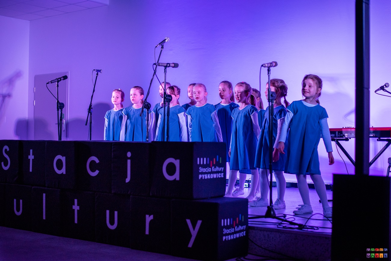 Zdjęcie przedstawia śpiewające dziewczynki na scenie oświetlonej na niebiesko