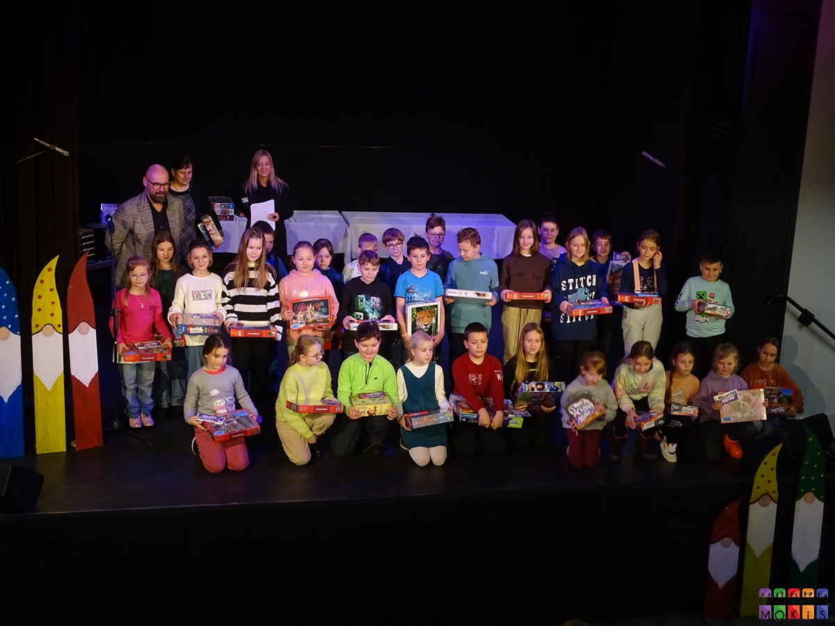 Zdjęcie przedstawiające wręczenie nagród dzieciom na scenie MOKiS-u przez Burmistrza miasta. Dzieci stojące z nagrodami w rękach ustawionymi do zdjęcia