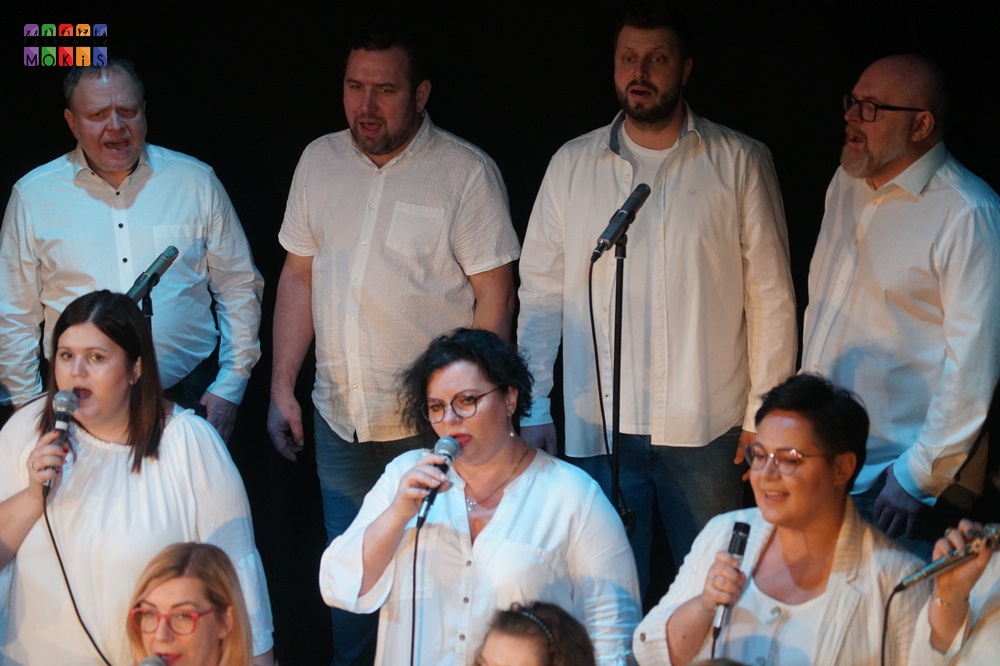 Zdjęcie przedstawia grupę ludzi śpiewających na scenie.
