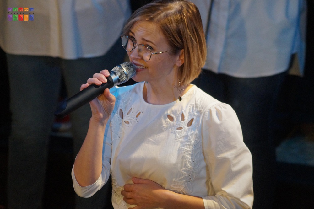 Zdjęcie przedstawia śpiewającą kobietę do mikrofonu