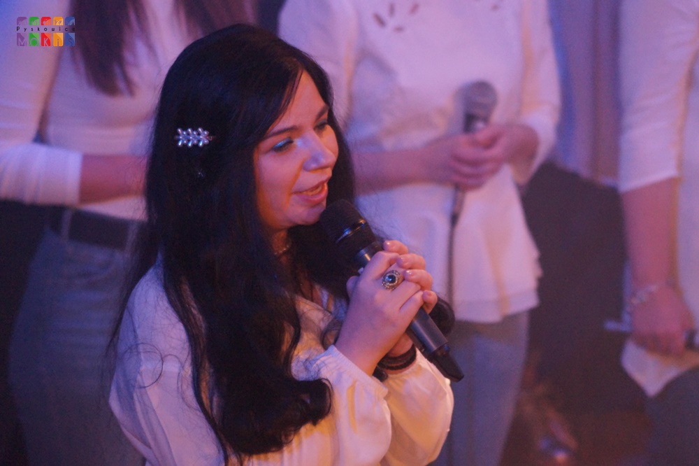 Zdjęcie przedstawia wokalistkę śpiewającą do mikrofonu.