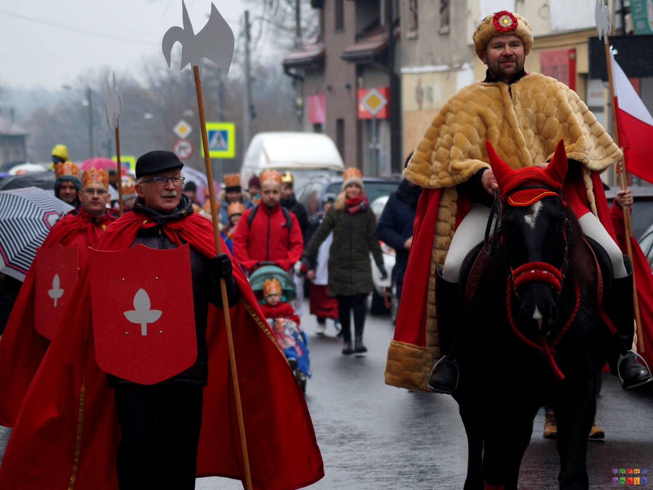 Zdjęcie przedstawiające Orszak Trzech Króli. Idący i stojący ludzie przebranych za króli. jeden z nich siedzi na koniu.