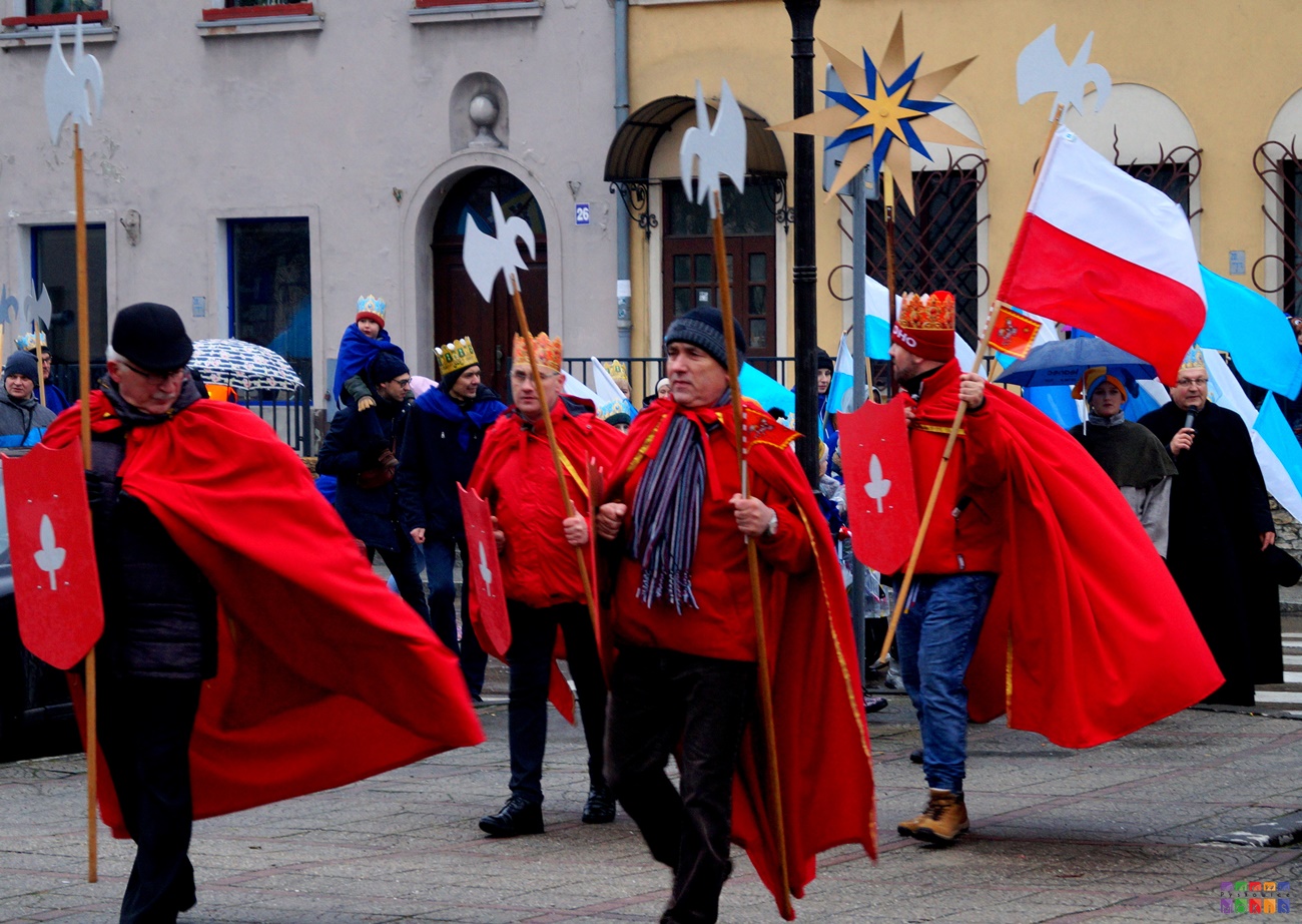 Zdjęcie przedstawiające Orszak Trzech Króli. Idący i stojący ludzie przebranych za rycerzy W tle widać flagę Polską.