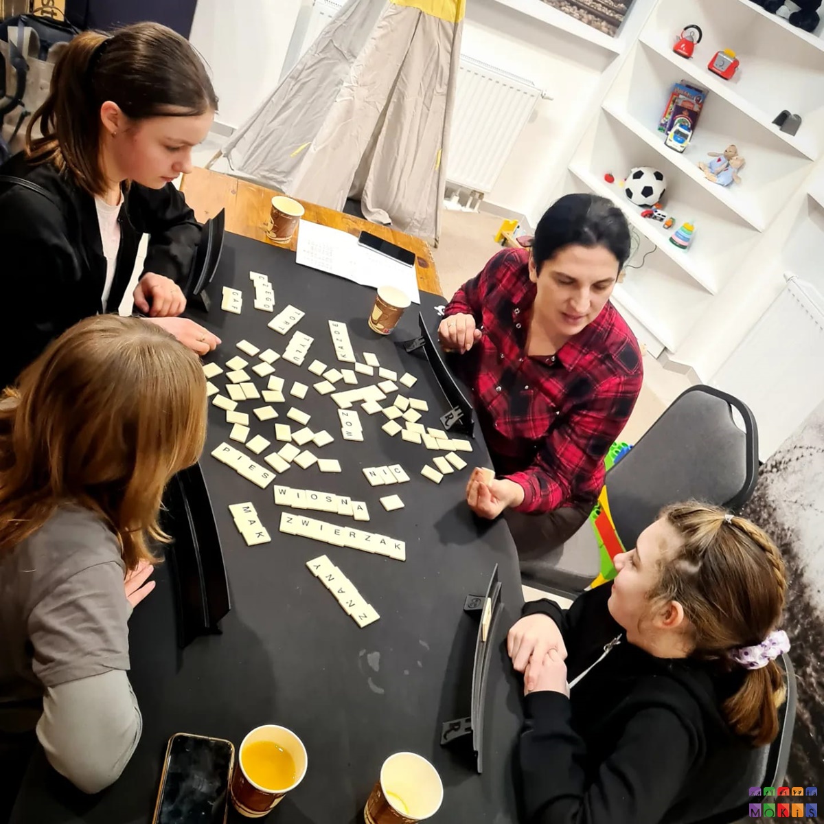 Zdjęcie przedstawiające grających ludzi w gry planszowe. Gry rozłożone są na stołach.